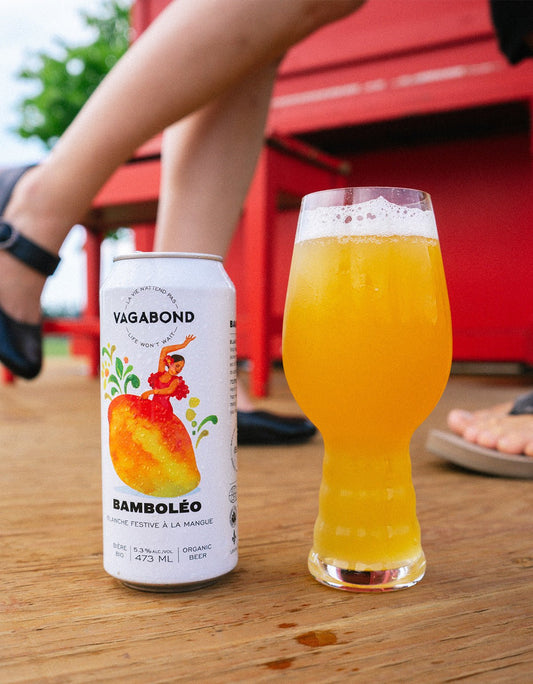 Canette et verre de bière Vagabond Bamboléo – blanche bio à la mangue 5.3%, photo estivale en extérieur sur fond rouge, bière fruitée et rafraîchissante
