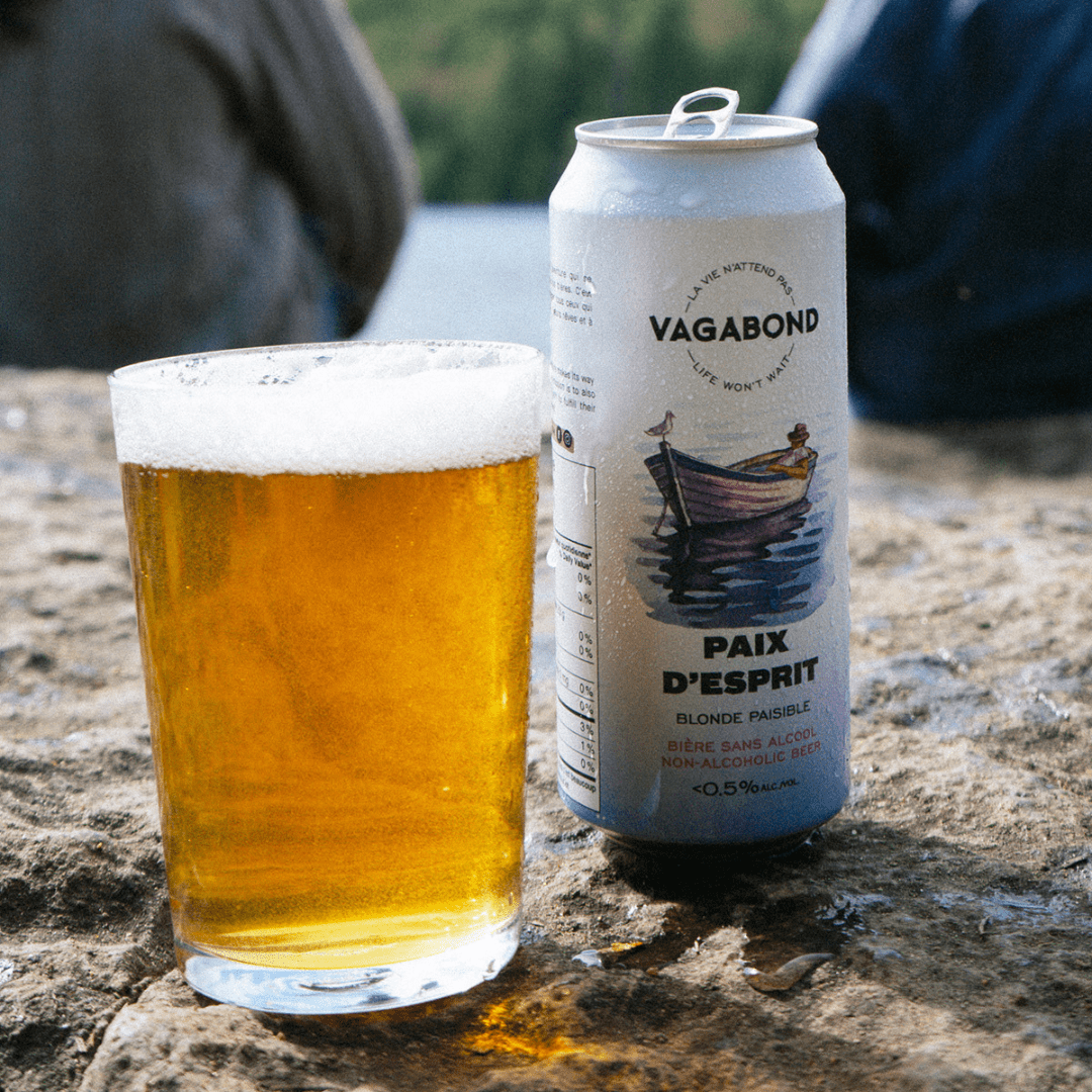 Canette de bière sans alcool Vagabond Paix d’Esprit avec un verre et des gens assis en arrière près d'un lac.