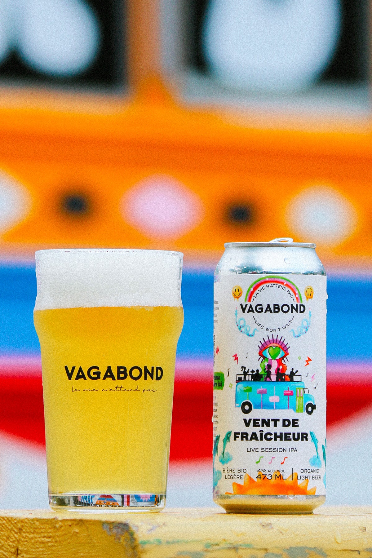Canette et verre de bière Vagabond Vent de Fraîcheur – Live Session IPA bio légère 4%, photo colorée d’ambiance festive et estivale devant un fond artistique multicolore.